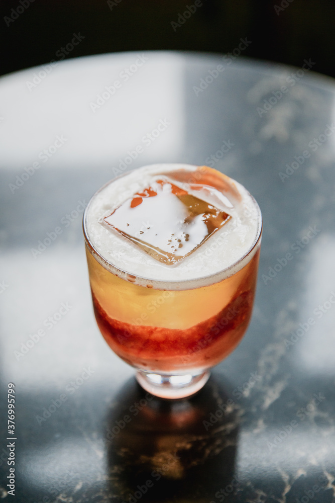 A beautiful pink cocktail with a big ice cube in a lowball glass, garnished with blood orange zest, a reflection in black marble table A beautiful pink cocktail with a big ice cube in a lowball glass, garnished with blood orange zest, a reflection in black marble table
