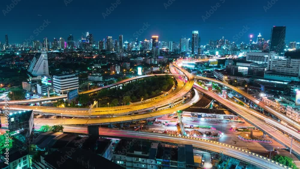 Time-lapse of car traffic transportation on highway road intersection in Bangkok city, Thailand at night. Public transport, commuter lifestyle, Asian city life concept. High angle view, zoom out
