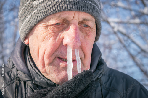 The man's snot was frozen in his nose. Portrait of an elderly man with icicles in his nose. Runny nose in the winter forest. Frosty weather in winter. Comic concept of a winter cold.