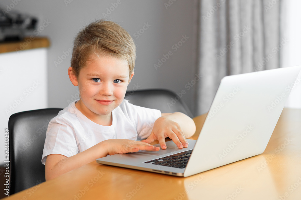 Funny young boy using a laptop computer sitting on top of a tableundefined at home