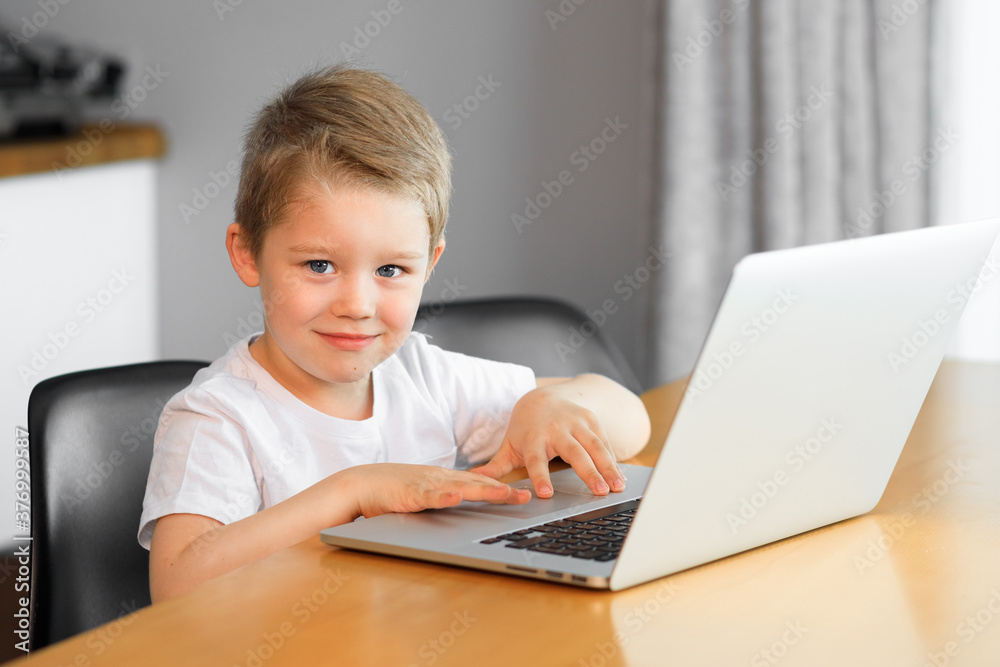 Funny young boy using a laptop computer sitting on top of a tableundefined at home Funny young boy using a laptop computer sitting on top of a tableundefined at home