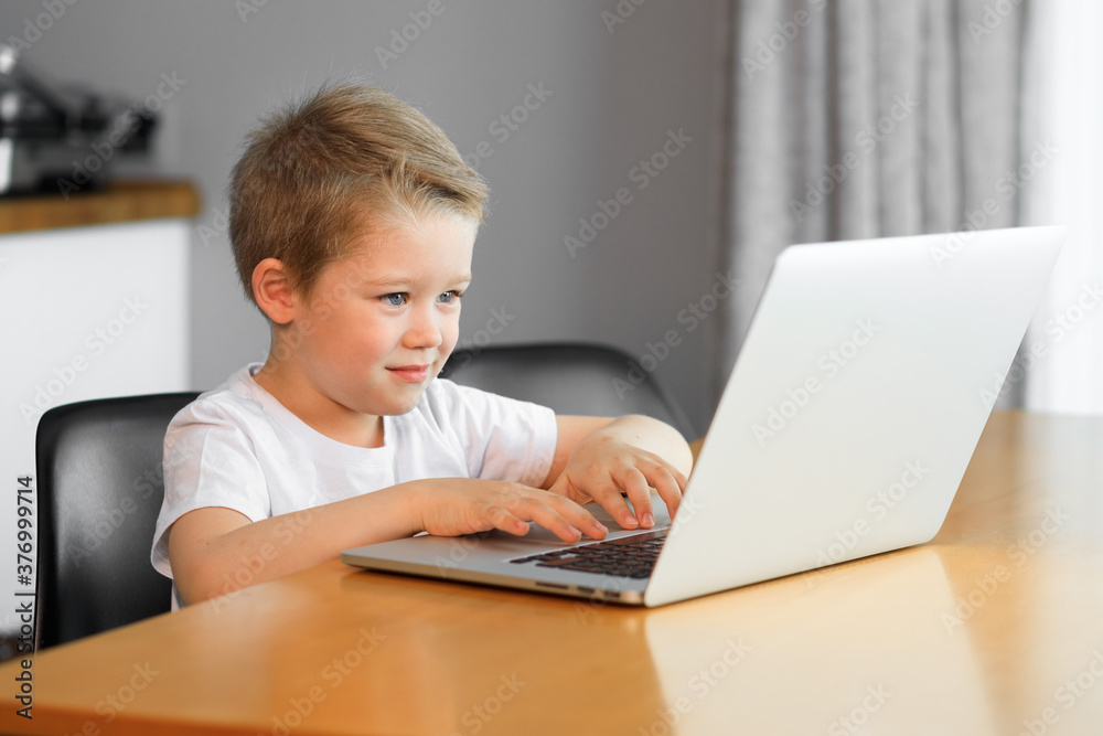 Funny young boy using a laptop computer sitting on top of a tableundefined at home Funny young boy using a laptop computer sitting on top of a tableundefined at home
