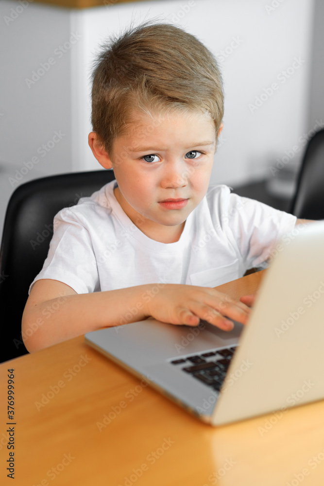A young boy using a laptop computer sitting on top of a tableundefined at home A young boy using a laptop computer sitting on top of a tableundefined at home