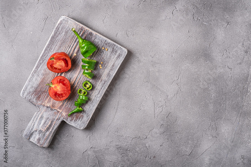 Sliced fresh ripe tomatoes with hot chili peppers on old wooden cutting board, stone concrete background, top view copy space