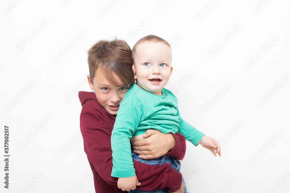 Two boys with a smile on a white background. The older brother hugs the younger Two boys with a smile on a white background. The older brother hugs the younger