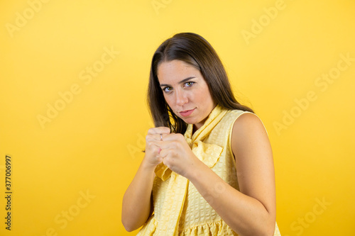 Young beautiful woman over isolated yellow background Punching fist to fight, aggressive and angry attack, threat and violence