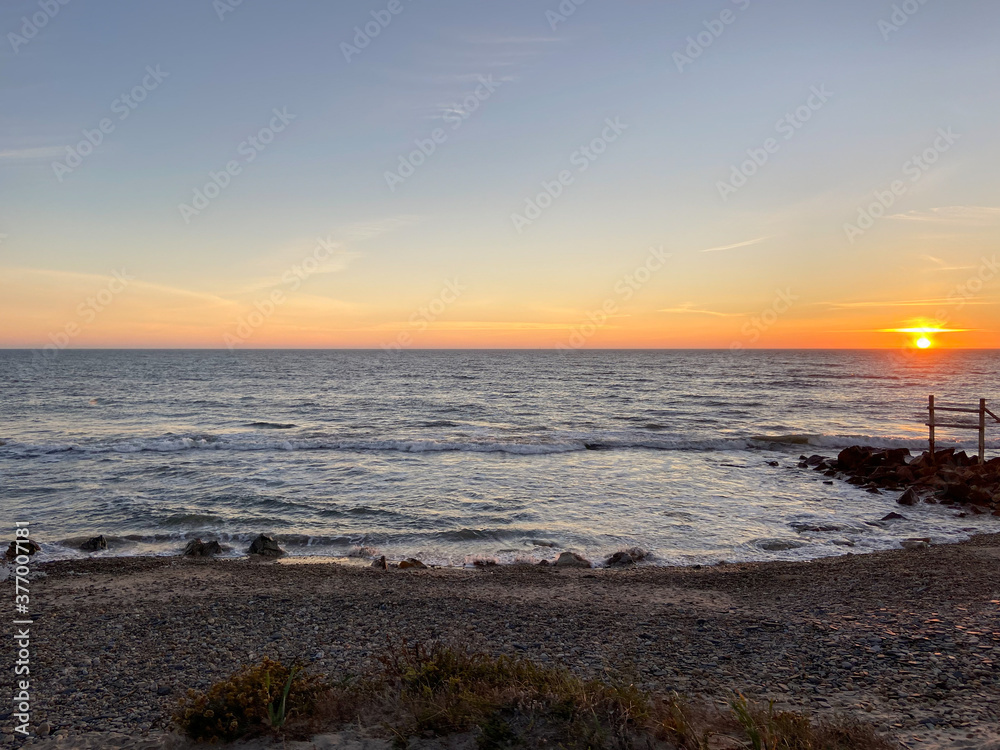Obraz premium Sea, beach boulders, pebble shore and waves at sunset. Sea waves breaking on rocks. Beach with sand dunes and dusk sky in Esposende, Portugal.