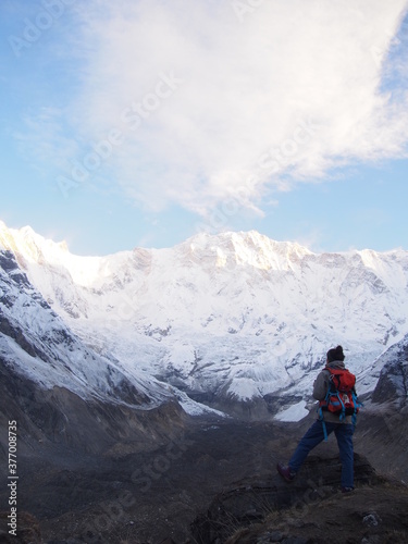 A mountain climber standing on a rock near the top and watches the sunrise over a snow-covered rock, ABC (Annapurna Base Camp) Trek, Annapurna, Nepal