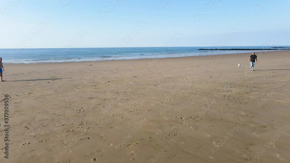 Knokke, Belgium - drone shot of two men playing football at the beach. Knokke, Belgium - drone shot of two men playing football at the beach.