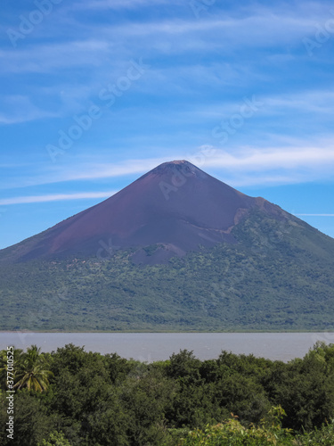 Leon, Nicaragua - November 27, 2008: Ruins of old Leon. Portrait of Momotombo volcano mountain seen from the ruins under blue sky with white stripes. Brown water of lake Xolotian.
