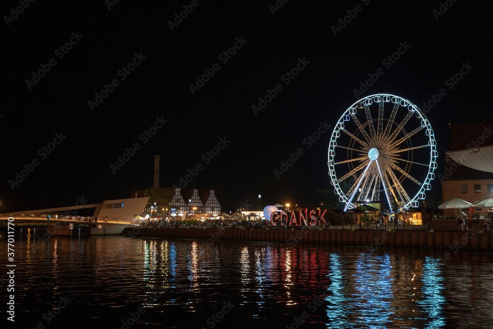 Gdansk, North Poland - August 13, 2020: Night photography of cityscape consisting old town commercial market and illuminated ferries wheel over motlawa river