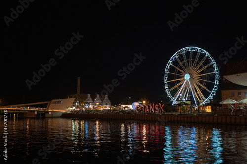 Gdansk, North Poland - August 13, 2020: Night photography of cityscape consisting old town commercial market and illuminated ferries wheel over motlawa river
