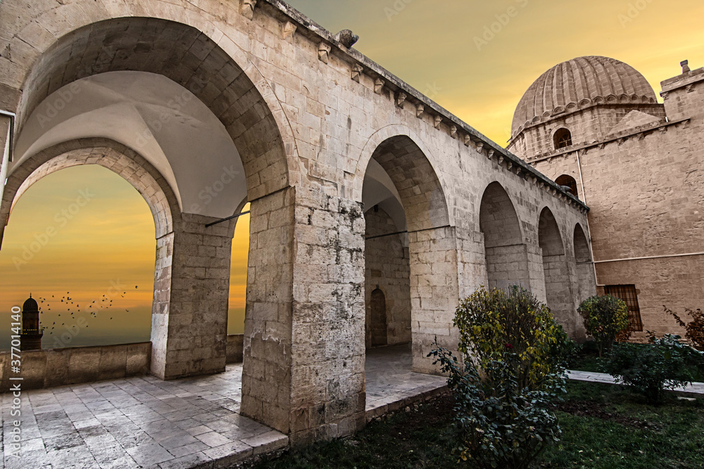 zinciriye madrasah mardin, birds are being seen from the arches of the old building, garden of an old building, stone arches and orange sky