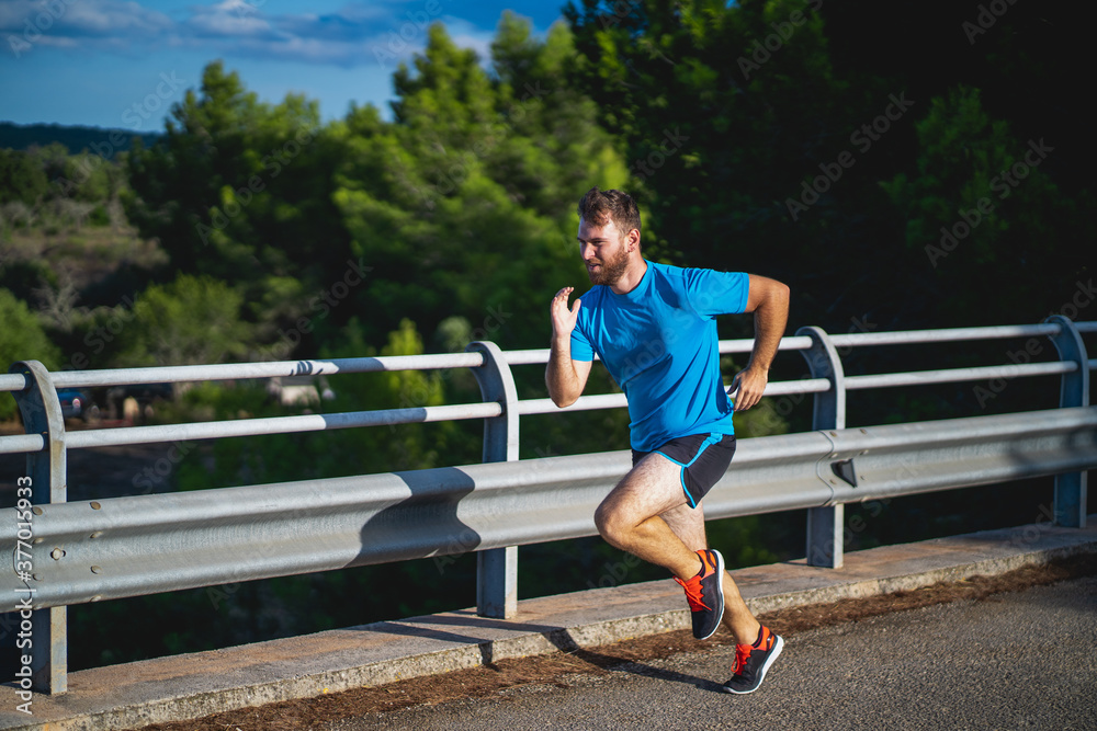 Young man takes a sprint over a highway bridge an hour before sunset surrounded by nature in Mallorca (Spain)