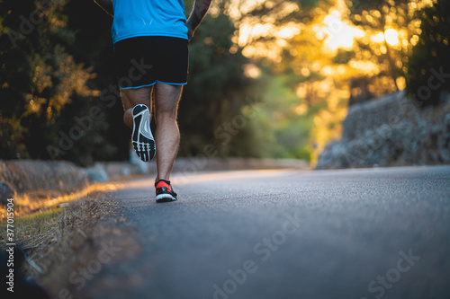 Young man wearing blue shirt and black shorts runs on an idyllic road during sunset surrounded by nature in Mallorca (Spain)