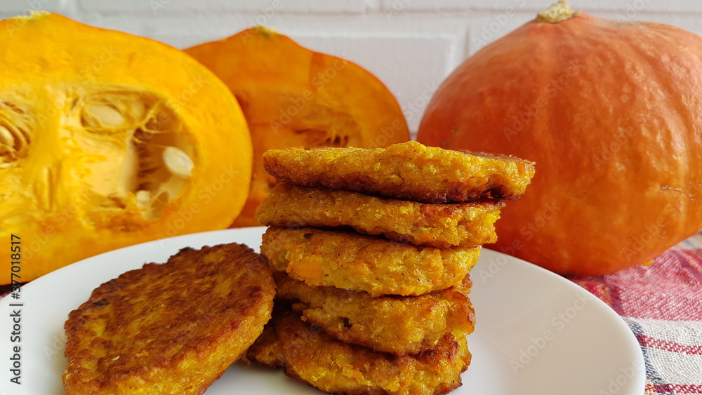 Pumpkin cutlets on a white plate against a background of a white brick wall and two halves of a pumpkin and one whole pumpkin Pumpkin cutlets on a white plate against a background of a white brick wall and two halves of a pumpkin and one whole pumpkin