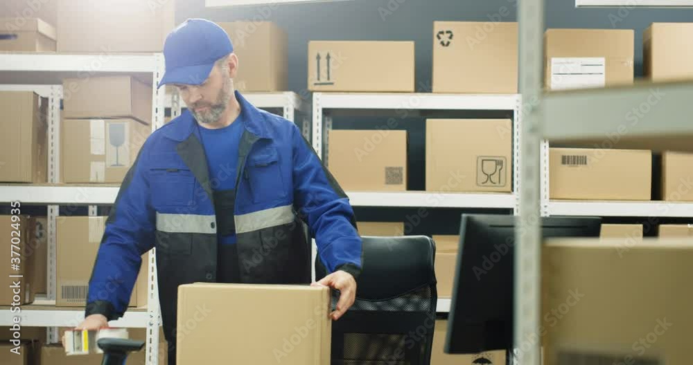 Caucasian postal male worker in uniform packing carton box on table and handing parcel to camera at delievery department in post office. Postman closing mail with sticky tape. Mailing concept. Caucasian postal male worker in uniform packing carton box on table and handing parcel to camera at delievery department in post office. Postman closing mail with sticky tape. Mailing concept.
