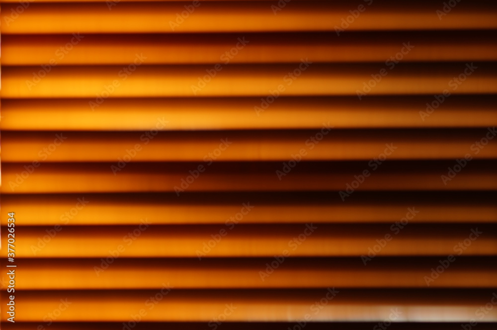 Abstract background - wooden blinds on the window, large brown-golden horizontal stripes lit by the sun