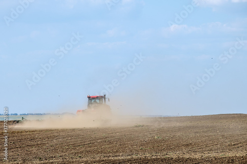 A red farm tractor in a cloud of dust cultivates the soil in the field with a cultivator after harvest. Summer sunny day. Fertile land. Modern agricultural machinery. Copy space. High quality photo © Nekrasov
