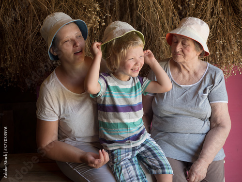 Beautiful elderly woman with wrinkles, young girl and boy from same family. Three different ages of similar people. mother, adult daughter and grandson in identical hats on background of dry flowers