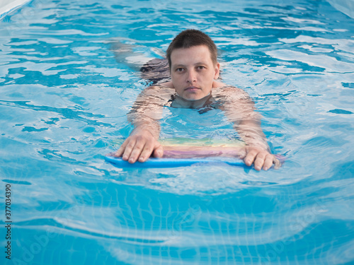sports girl with short haircut swims on LGBT multi-colored board for swimming in frame pool for country house. Sunny summer day. concept of family vacations and active lifestyle after quarantine © galitsin