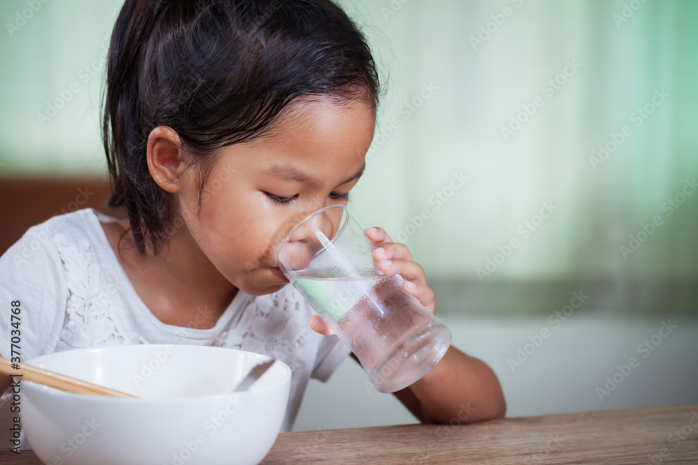 Cute asian child girl eating delicious instant noodles and drinking the glass of water for her lunch in the house Cute asian child girl eating delicious instant noodles and drinking the glass of water for her lunch in the house