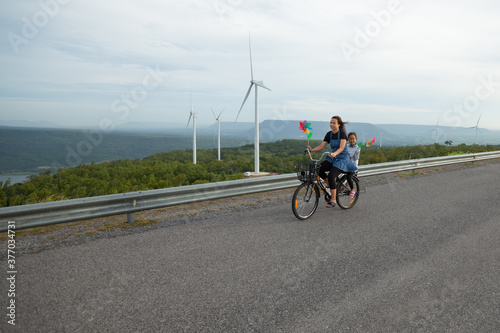 Asian child girl and mother riding bicycle and playing in the wind turbine field with fun together