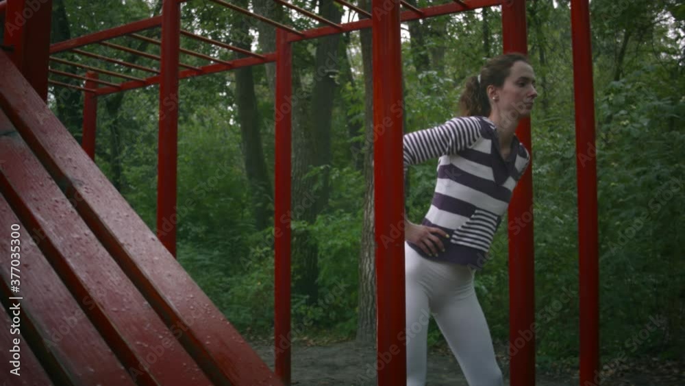 Young caucasian woman doing sports on the playground in the forest on a cloudy day. Woman doing exercise on the sports ground. Young caucasian woman doing sports on the playground in the forest on a cloudy day. Woman doing exercise on the sports ground.