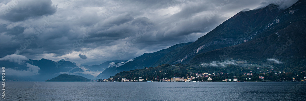 Landscape of dark lake Como with very cloudy sky and mountains, which is located in Northern Italy.