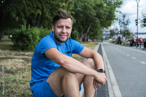 handsome male athlete in blue sportswear looks directly at the camera and smiles after an outdoor workout.