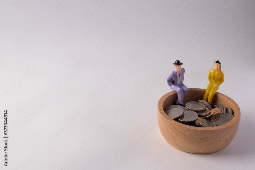 Fototapeta Miniature people. Sitting on a wooden bowl with coins on a white background. Money saving concept. Copy space.