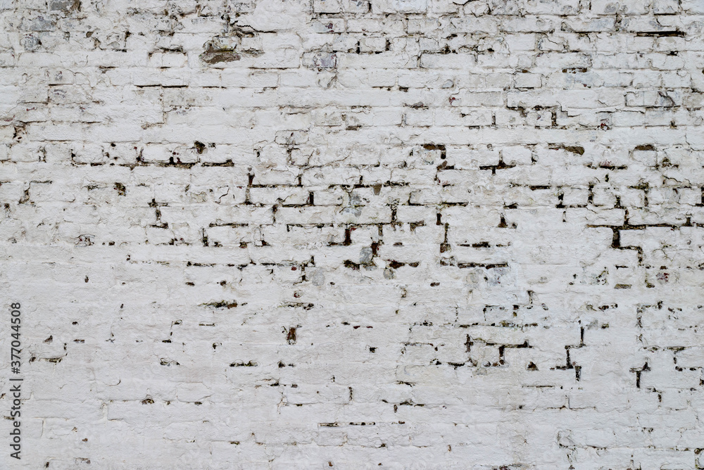 The texture of the old brick wall painted white with peeling paint