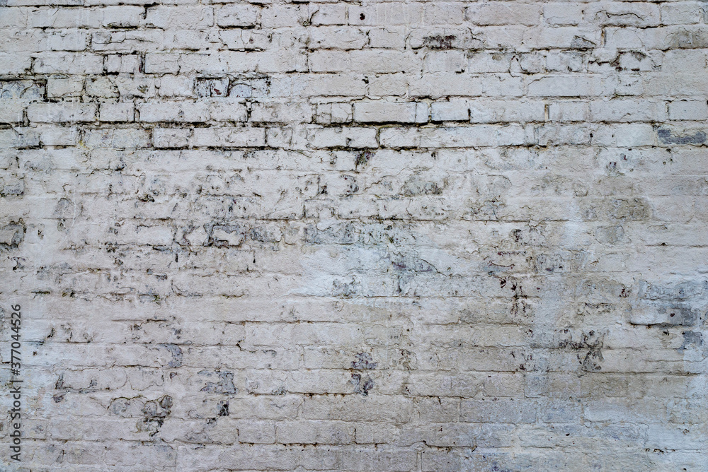 The texture of the old brick wall painted white with peeling paint
