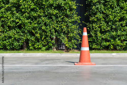 Fototapeta Naklejka Na Ścianę i Meble -  Single orange traffic cone on concrete street road with small park in background