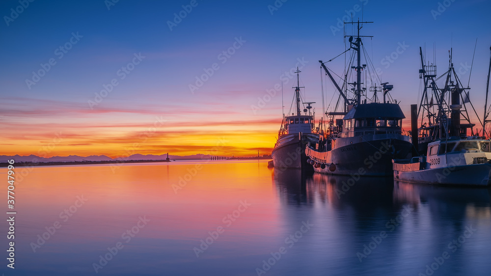 Fototapeta premium Seashore bay view with colourful sunset blue purple orange sky and clouds boats ships in dock
