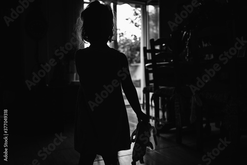 Little girl against the light with her rag doll in her hand in a scary wall. Halloween horror concept