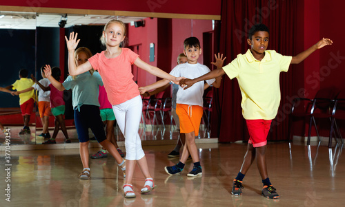 Smiling positive children primary school trying dancing salsa dance in modern studio