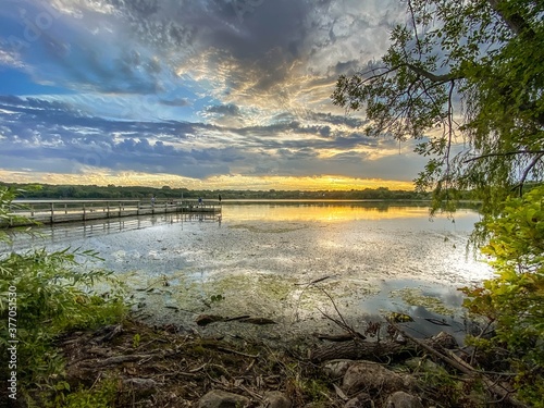 Dramatic sunset with cloudy sky over a Minnesota lake filled with green lily pads by a fishing dock in the summer 