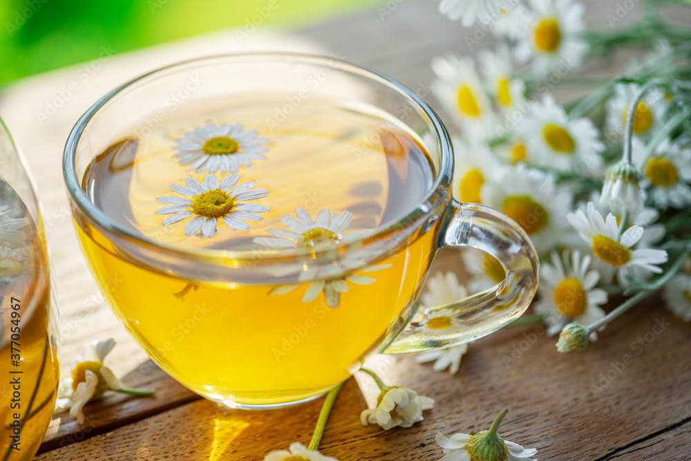 Herbal chamomile tea and chamomile flowers near teapot and tea glass on wooden table. Countryside background. Herbal chamomile tea and chamomile flowers near teapot and tea glass on wooden table. Countryside background.