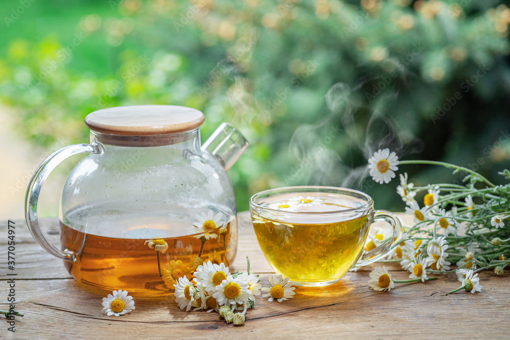 Herbal chamomile tea and chamomile flowers near teapot and tea glass on wooden table. Countryside background. Herbal chamomile tea and chamomile flowers near teapot and tea glass on wooden table. Countryside background.