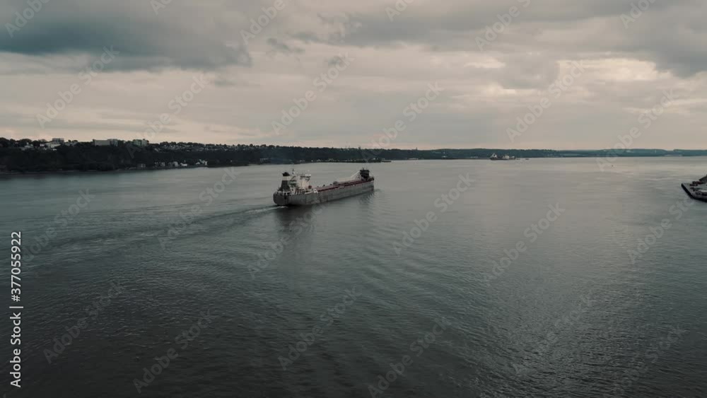 A Cargo Ship Sailing Across The Saint Lawrence River In Quebec, Canada Under The Dramatic Sky - aerial drone, panning shot