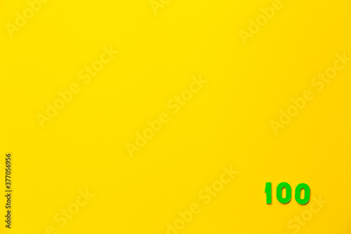 A green plastic toy number hundred is located in the lower right corner on a yellow background