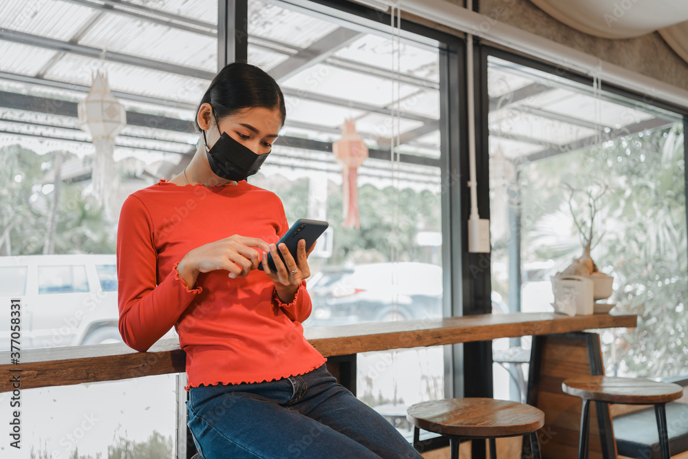 Happy traveller Asian woman with mask using mobile phone in village coffee shop, New normal lifestyle people due to outbreak of coronavirus in Thailand.