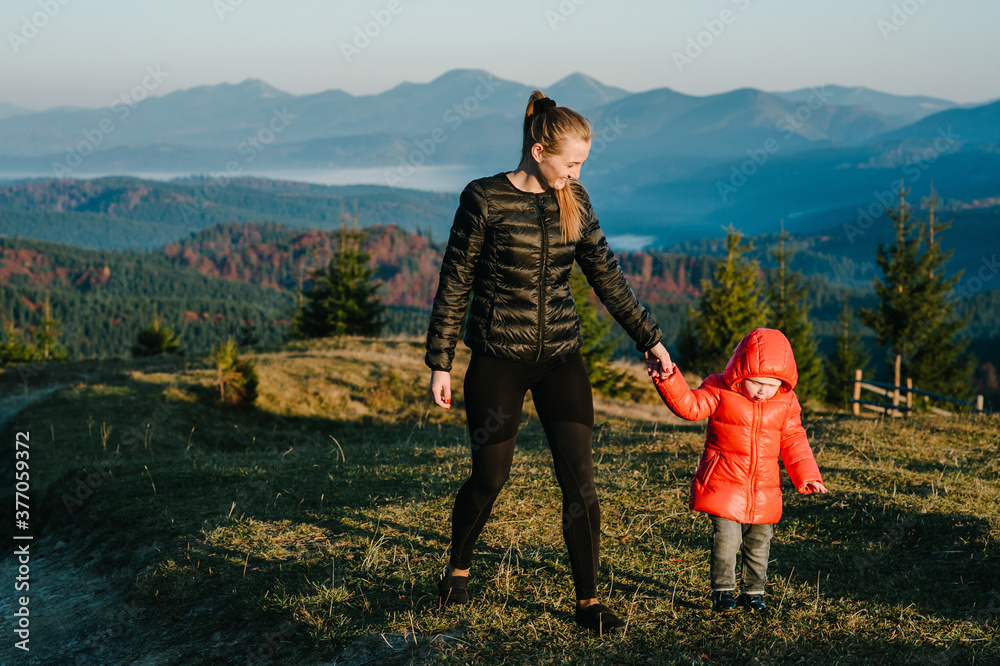Mother and daughter, enjoying time together, walking on sunset on top of foggy mountain. Tourists on background autumn nature. Hikers on sunlight in trip in country Europe. Happy family.