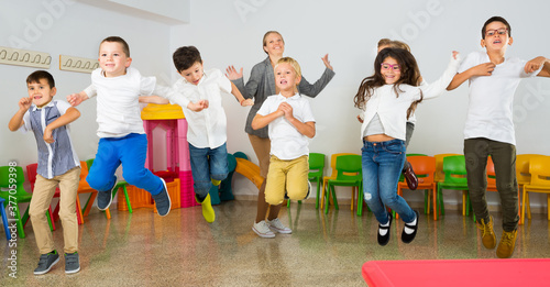 Group of happy cheerful children with their female teacher jumping together in the schoolroom