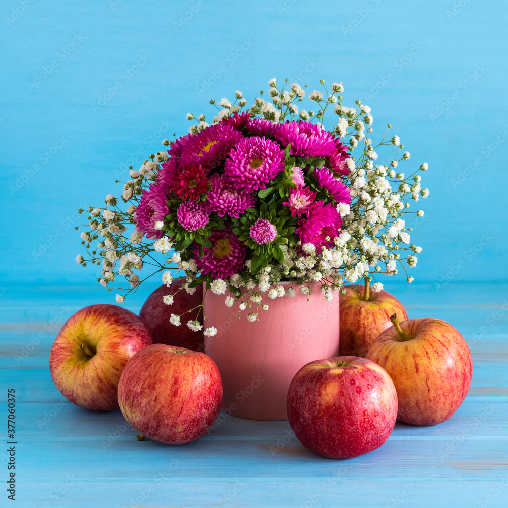 Autumn flowers and fresh apples on blue wooden background.