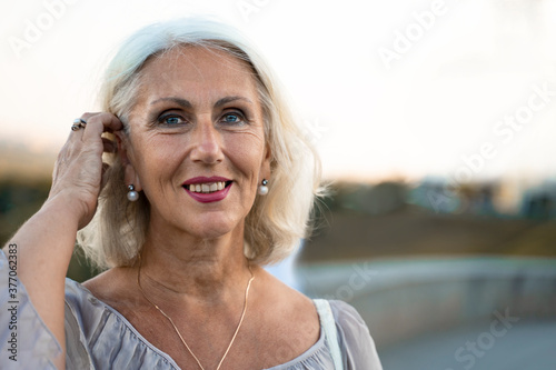 blue eyed caucasian woman in gray dress smiling and looking into the camera while standing in the park.