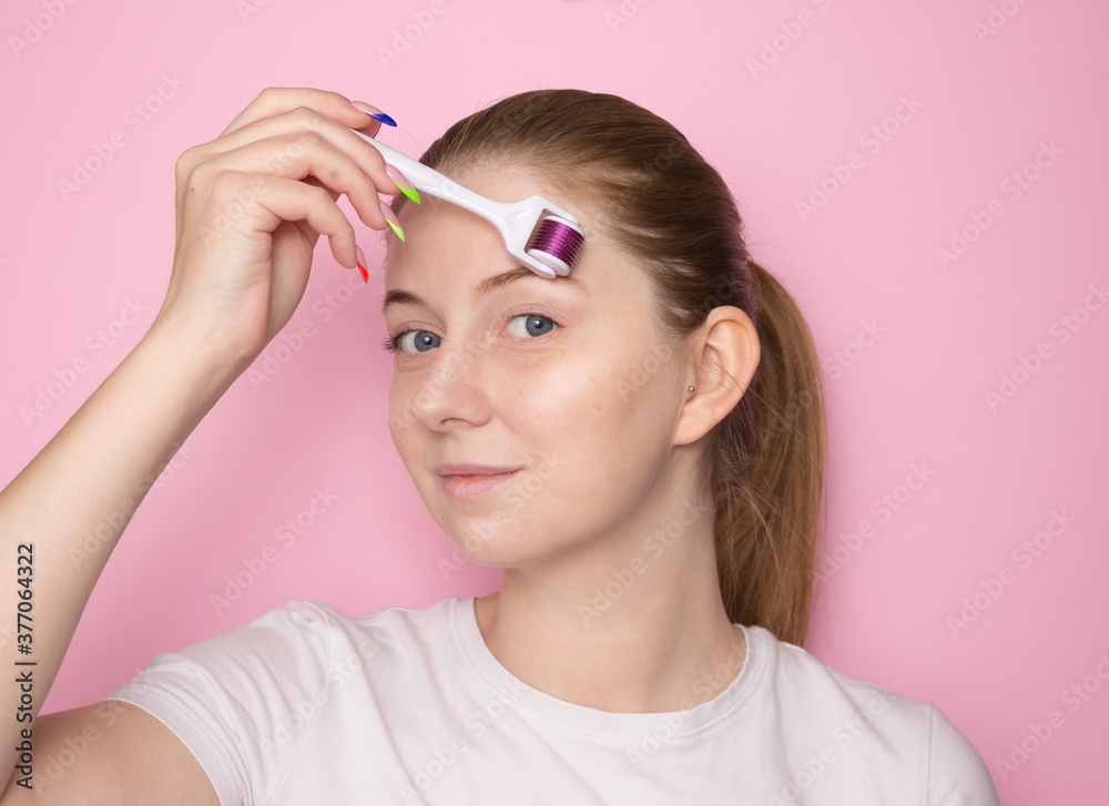 A woman's face on a pink background with a mesoroller. Facial skin care. Moisturizing, anti-aging care. A woman's face on a pink background with a mesoroller. Facial skin care. Moisturizing, anti-aging care.