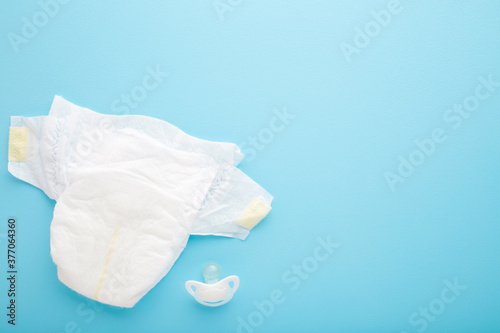 White baby diaper and soother on light blue table background. Pastel color. Closeup. Empty place for text. Top down view.