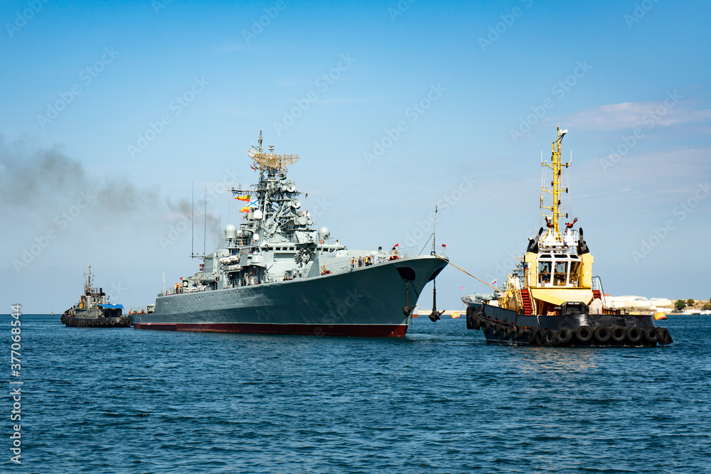 Large warship in the seaport. The ship is towed by two tugs.